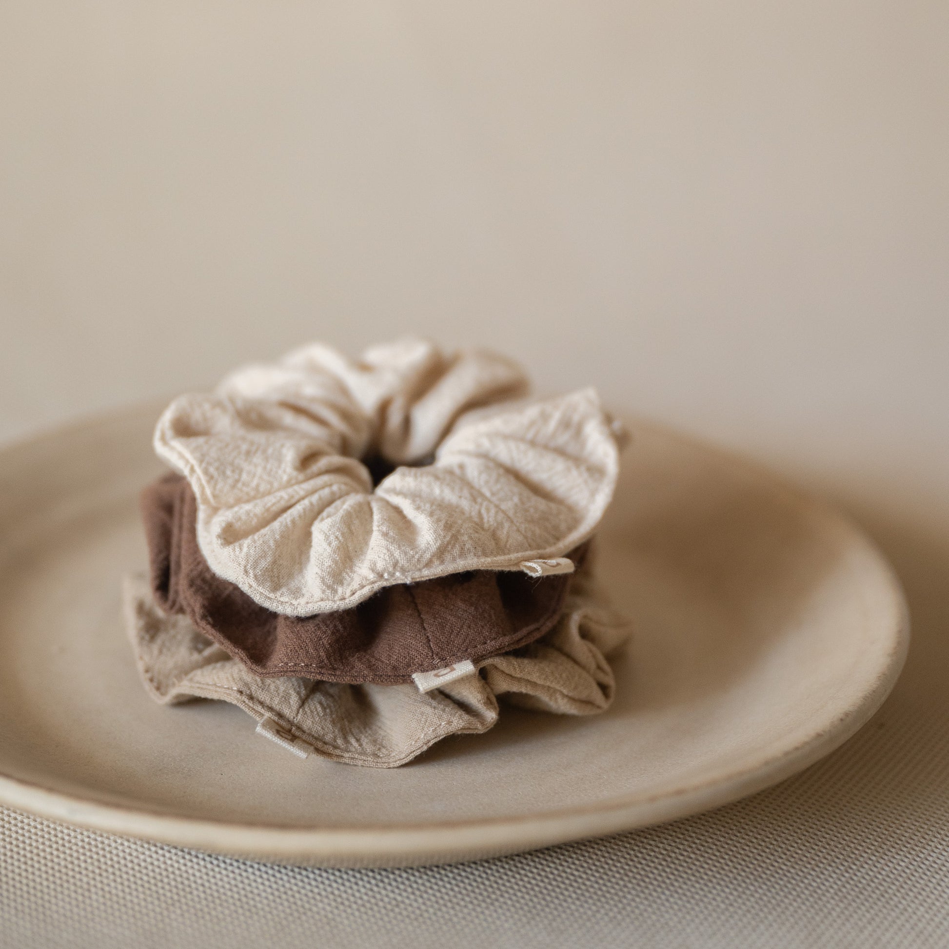 Pack of 3 crinkle cotton scrunchies in natural, wheat, and espresso tones, packaged in a mesh pouch.