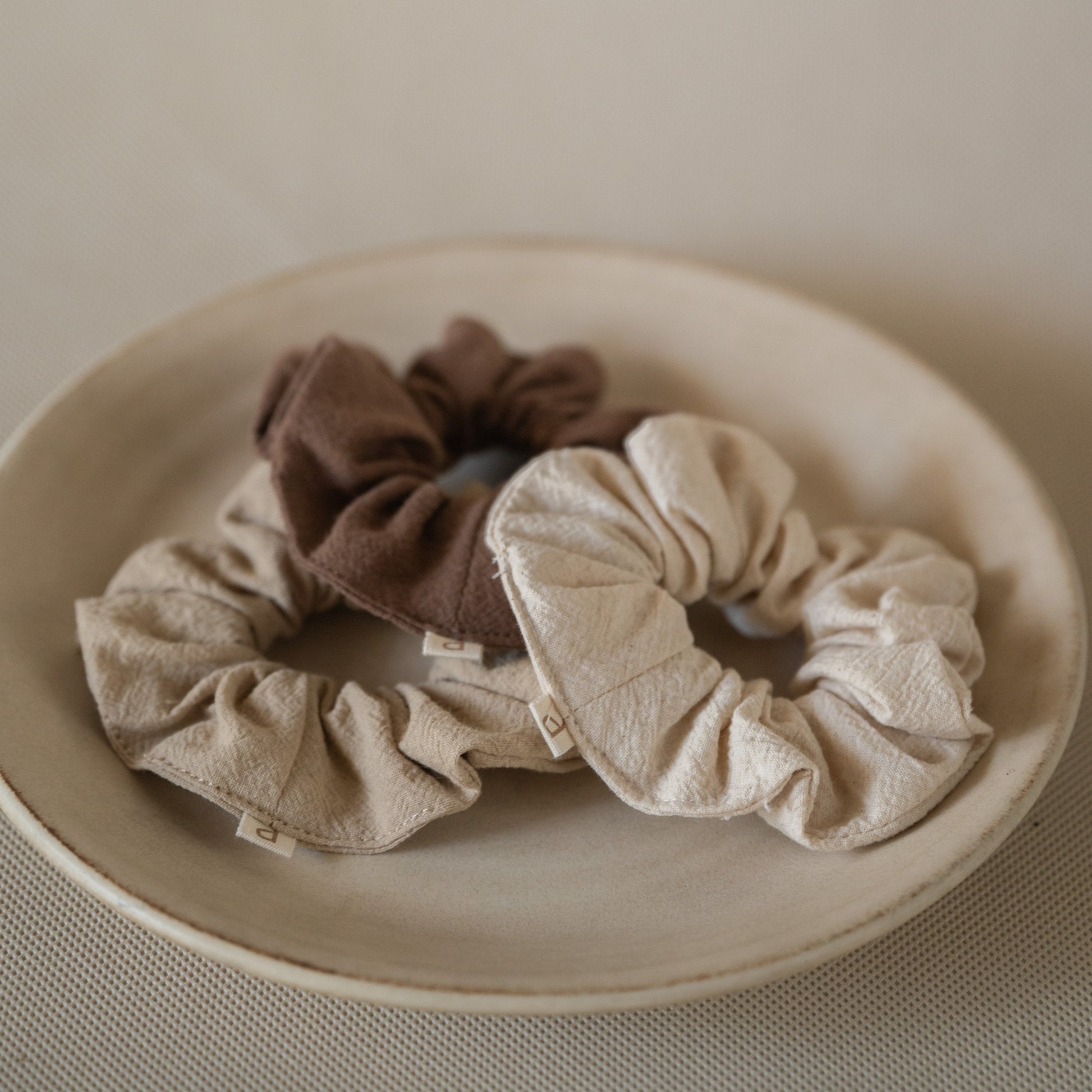 Pack of 3 crinkle cotton scrunchies in natural, wheat, and espresso tones, packaged in a mesh pouch.
