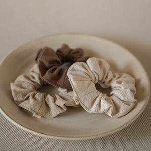 Pack of 3 crinkle cotton scrunchies in natural, wheat, and espresso tones, packaged in a mesh pouch.