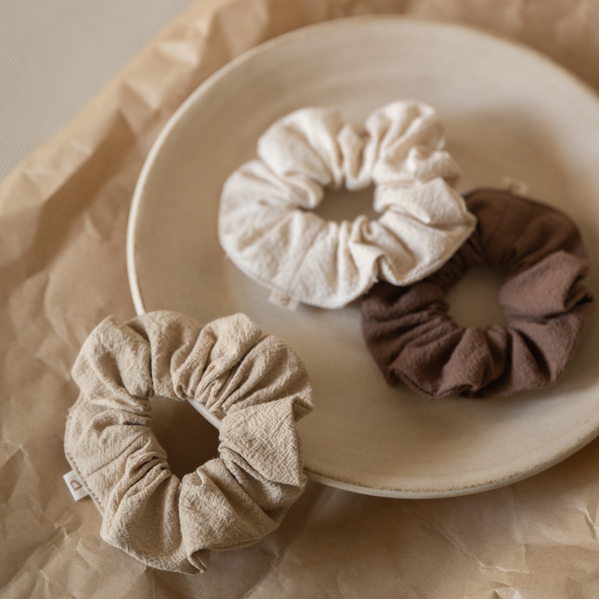 Pack of 3 crinkle cotton scrunchies in natural, wheat, and espresso tones, packaged in a mesh pouch.