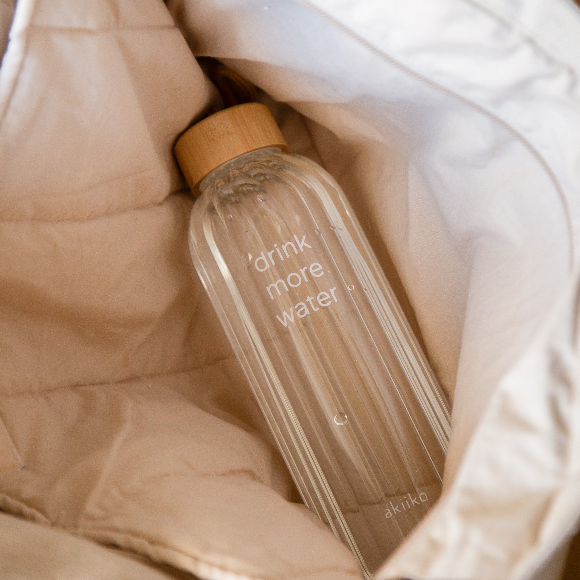 Transparent ribbed glass water bottle with “Drink More Water” text, bamboo lid, and rope handle, 750 ml.