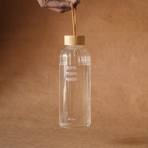 Transparent ribbed glass water bottle with “Drink More Water” text, bamboo lid, and rope handle, 750 ml.