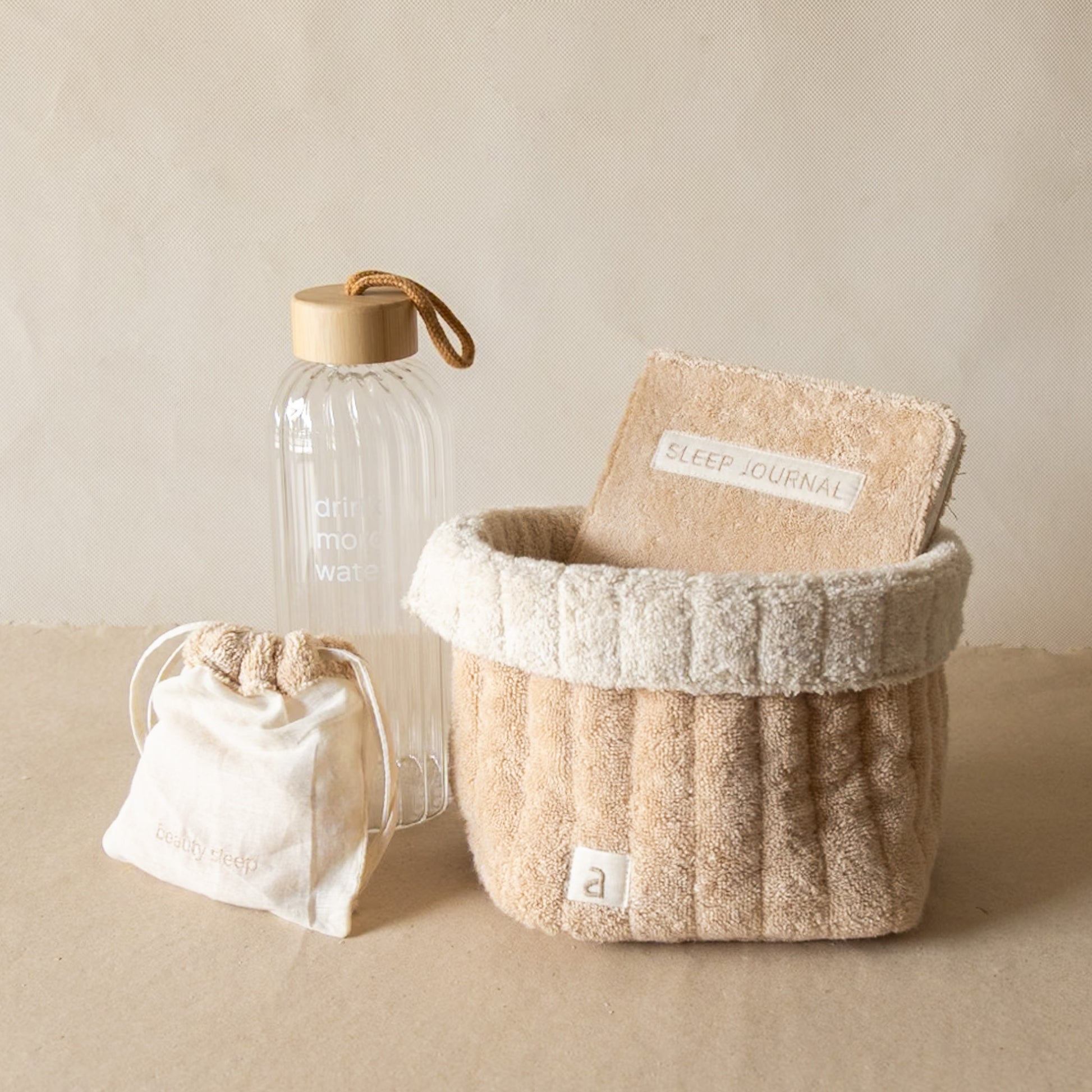 PM Cloud Self–Care Set featuring a foldover cloud terry basket with eyemask in drawstring pouch, terry sleep journal, and glass water bottle.