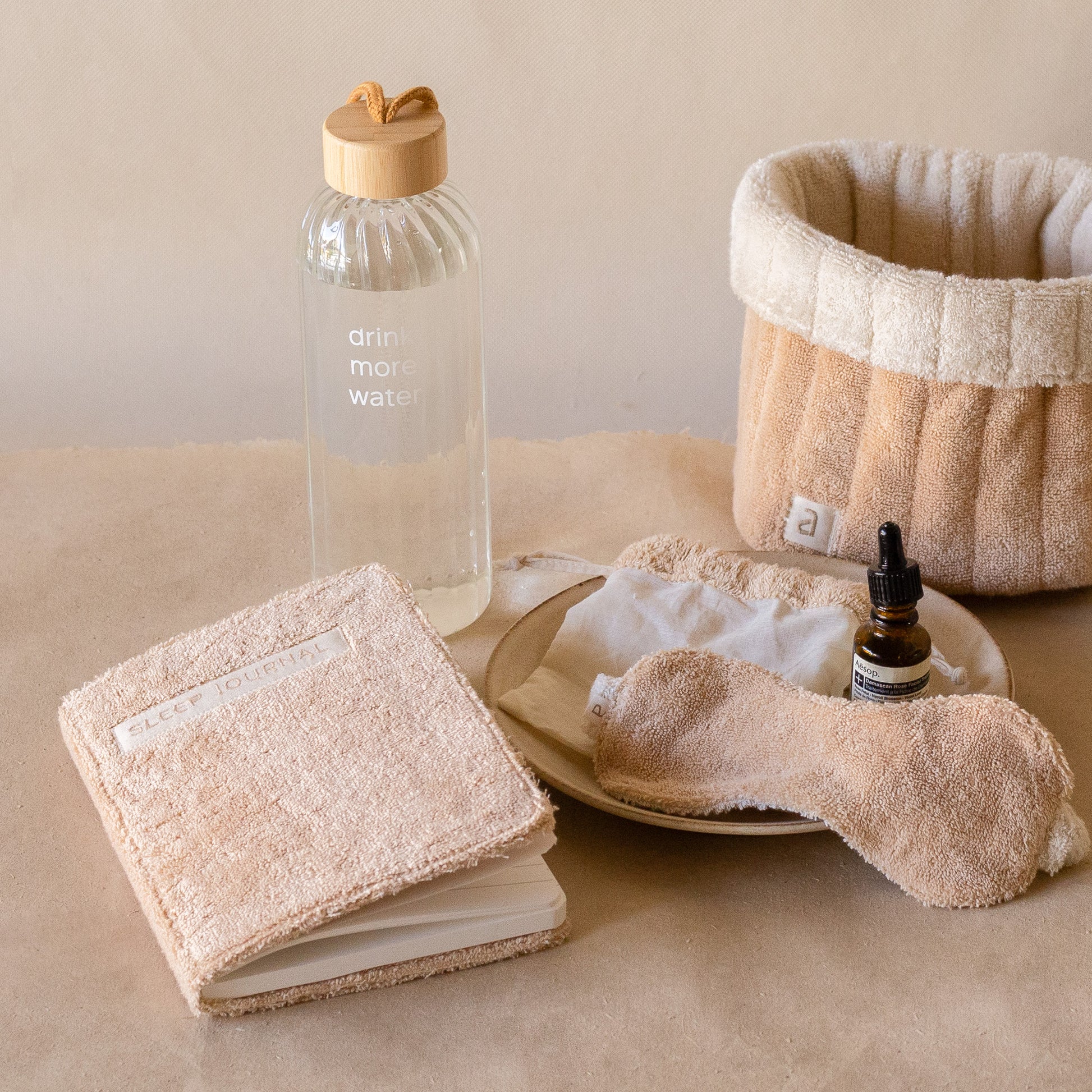 PM Cloud Self–Care Set featuring a foldover cloud terry basket with eyemask in drawstring pouch, terry sleep journal, and glass water bottle.