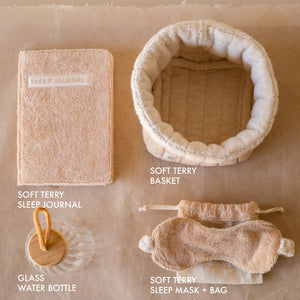 PM Cloud Self–Care Set featuring a foldover cloud terry basket with eyemask in drawstring pouch, terry sleep journal, and glass water bottle.