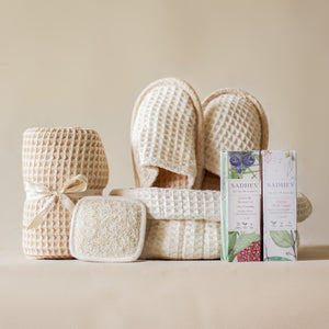 Soak & Soothe Bath Kit featuring Ayurvedic shower gel, body lotion, waffle luffa scrubber, latte waffle bath towel, cozy bath slippers, and a waffle storage basket.
