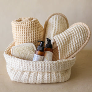 Soak & Soothe Bath Kit featuring Ayurvedic shower gel, body lotion, waffle luffa scrubber, latte waffle bath towel, cozy bath slippers, and a waffle storage basket.