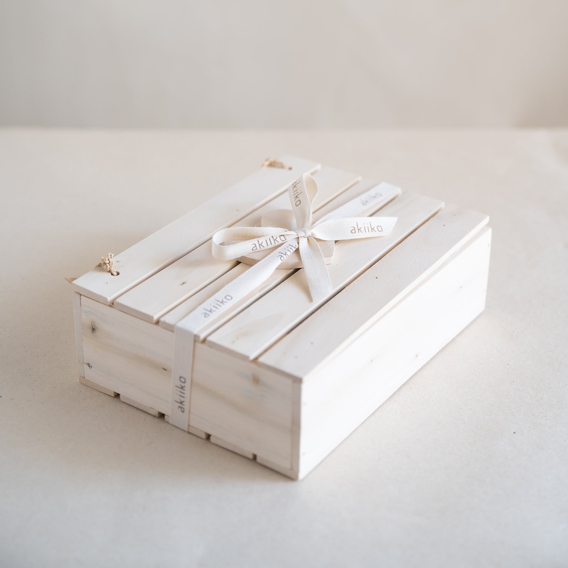 Wooden gift box containing a self-care set with two waffle hand towels, Sutachi scrunchie, six reusable facial rounds, bamboo comb, and a message card.